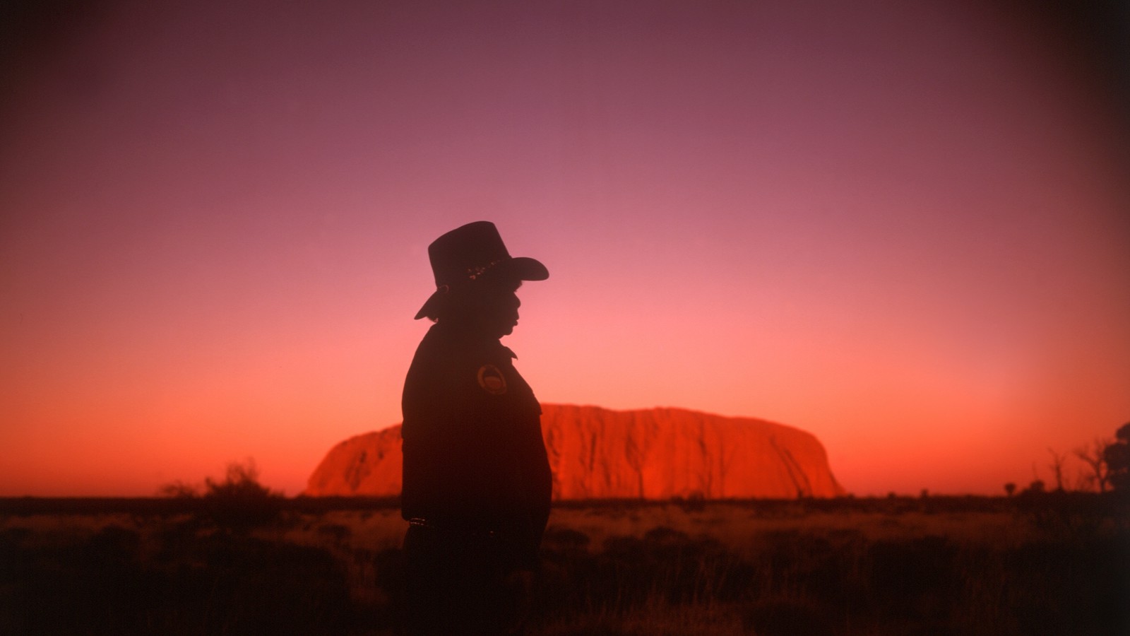Mann med hatt framför berg i solnedgång