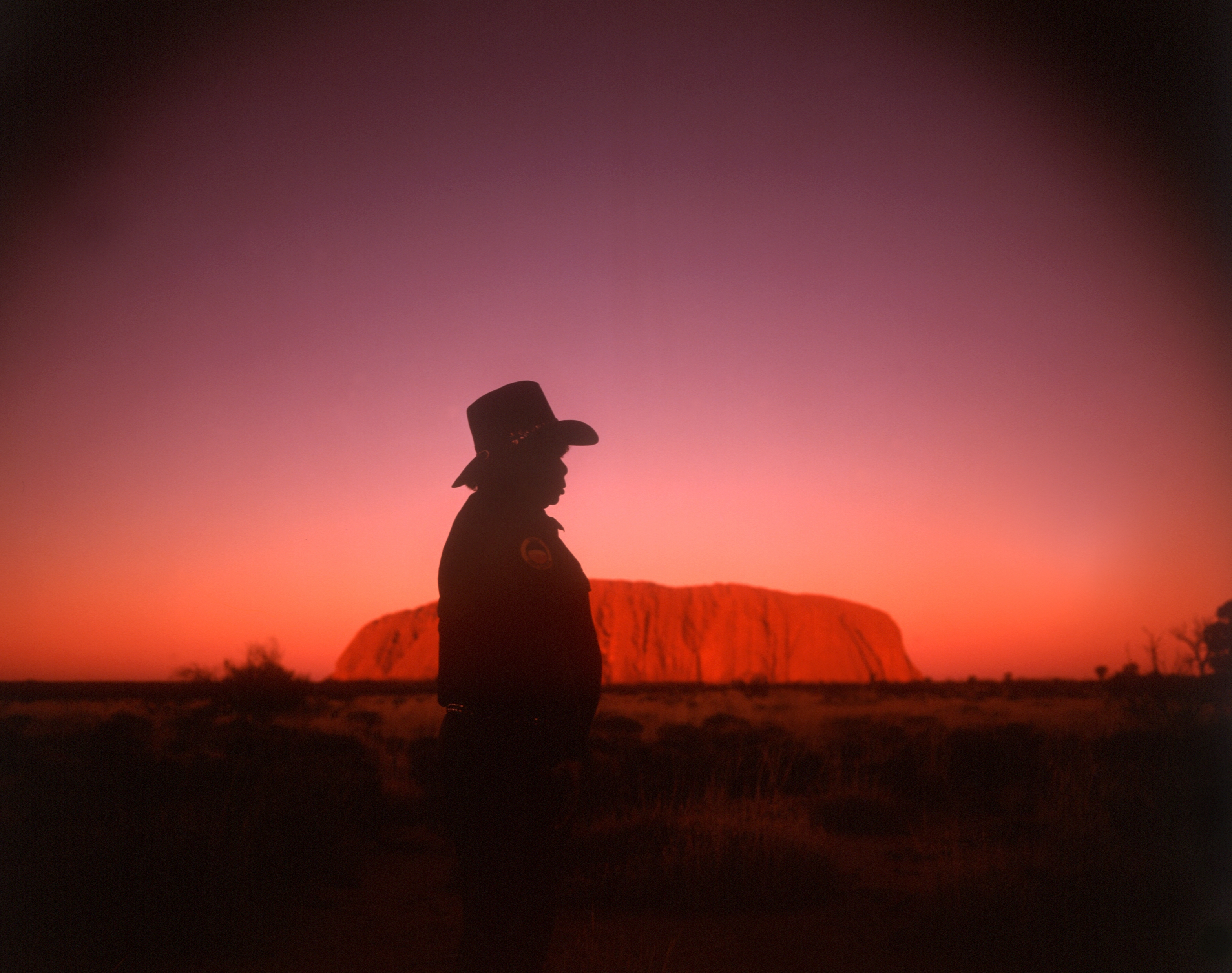 Mann med hatt framför berg i solnedgång