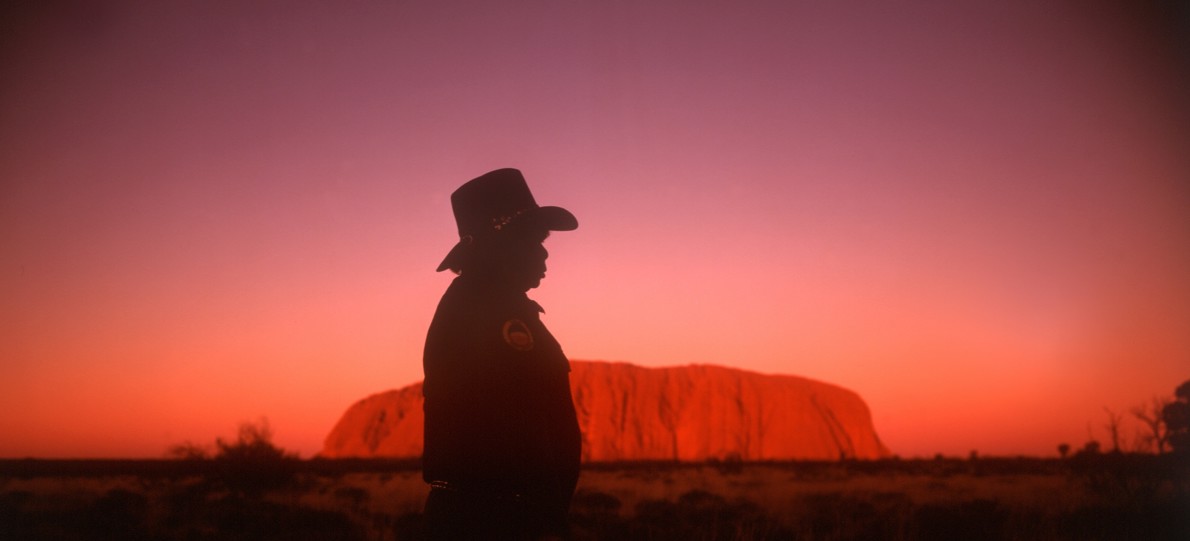 Mann med hatt framför berg i solnedgång